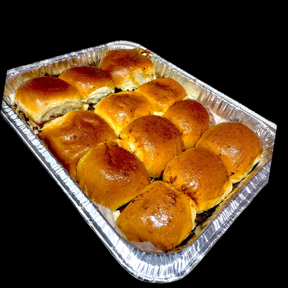 A foil tray filled with twelve golden-brown, glazed slider buns, likely from Gyro Flames.
