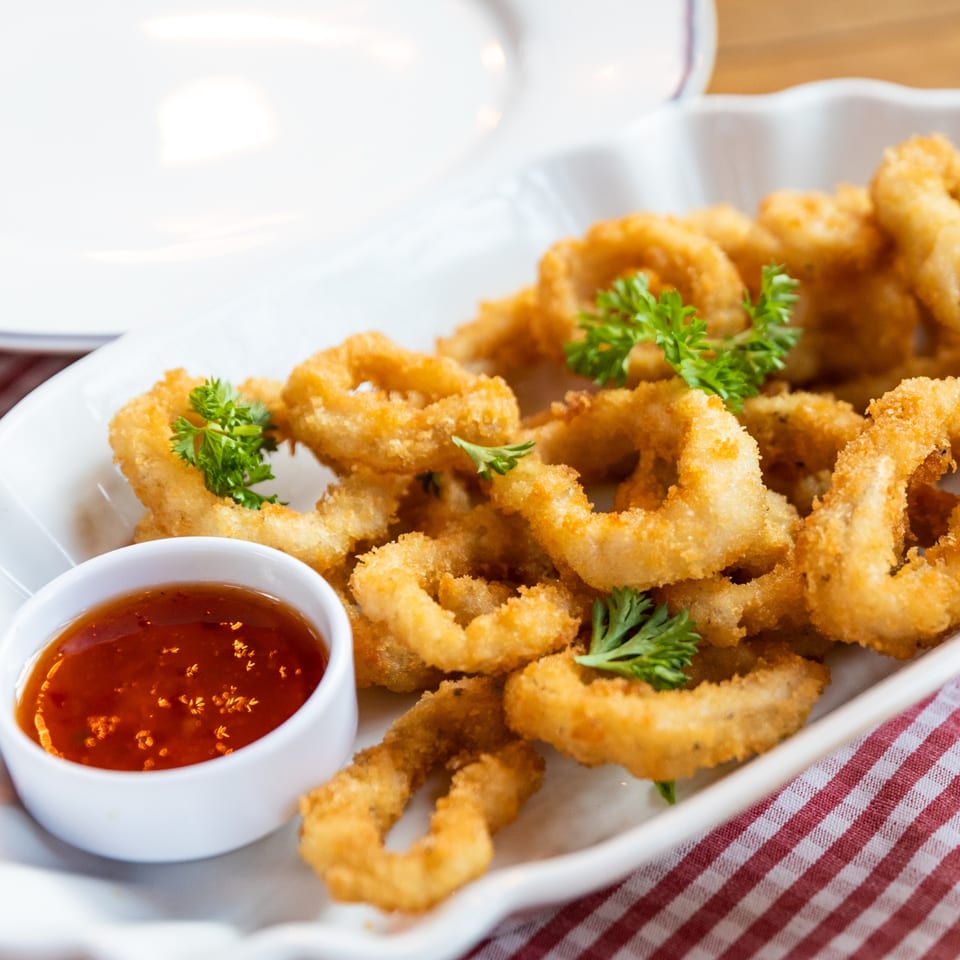Golden fried calamari rings with parsley garnish and a side of red dipping sauce on a white platter.
