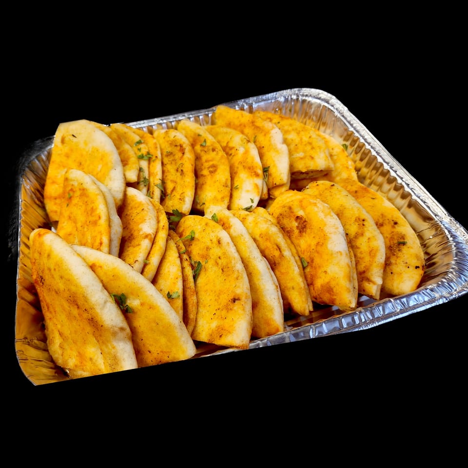 A foil tray filled with rows of golden-brown pita bread, lightly seasoned with herbs.